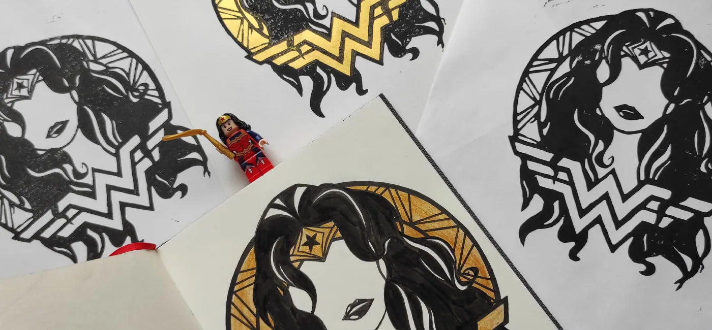 Impressions linogravure Wonder Woman noir et or étalées, figurine Lego Wonder Woman posée au centre