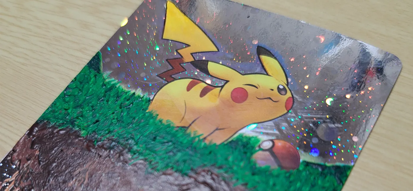 Gros plan carte Pokemon Pikachu customisée holographique, peinture acrylique débordante sur surface scintillante